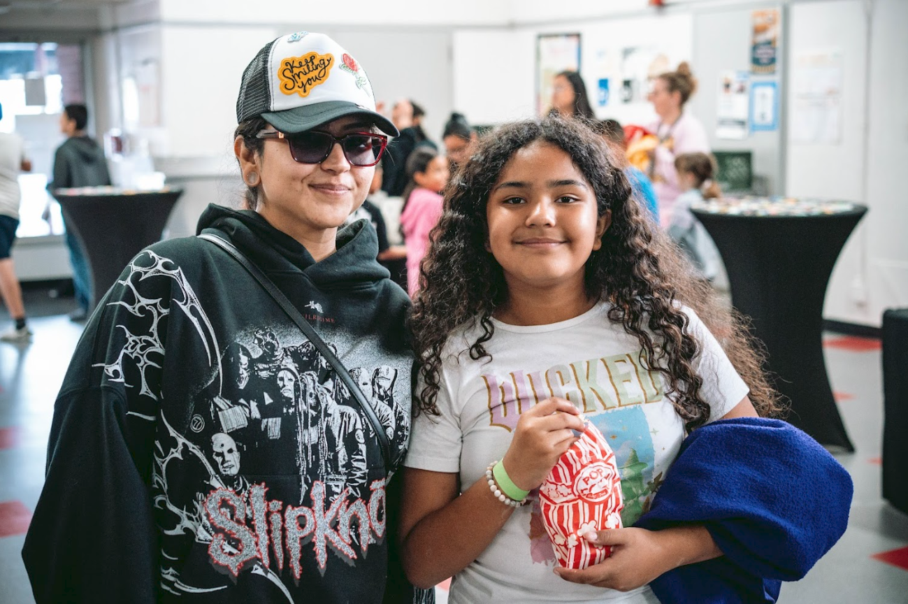 A woman and a girl posing with a movie popcorn in a crowded indoor location, possibly a theater or event hall.