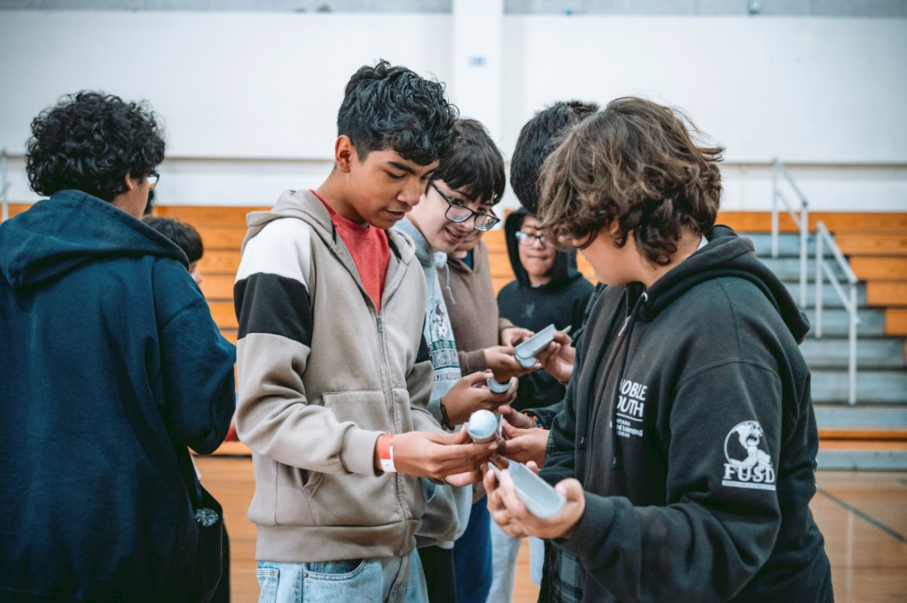 Group of teenagers in a gymnasium looking at and exchanging white rugby balls