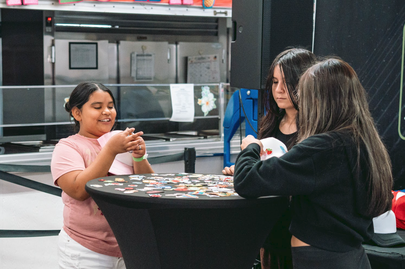 Three girls sitting around a round table playing a game with colorful chips or tokens in an indoor setting