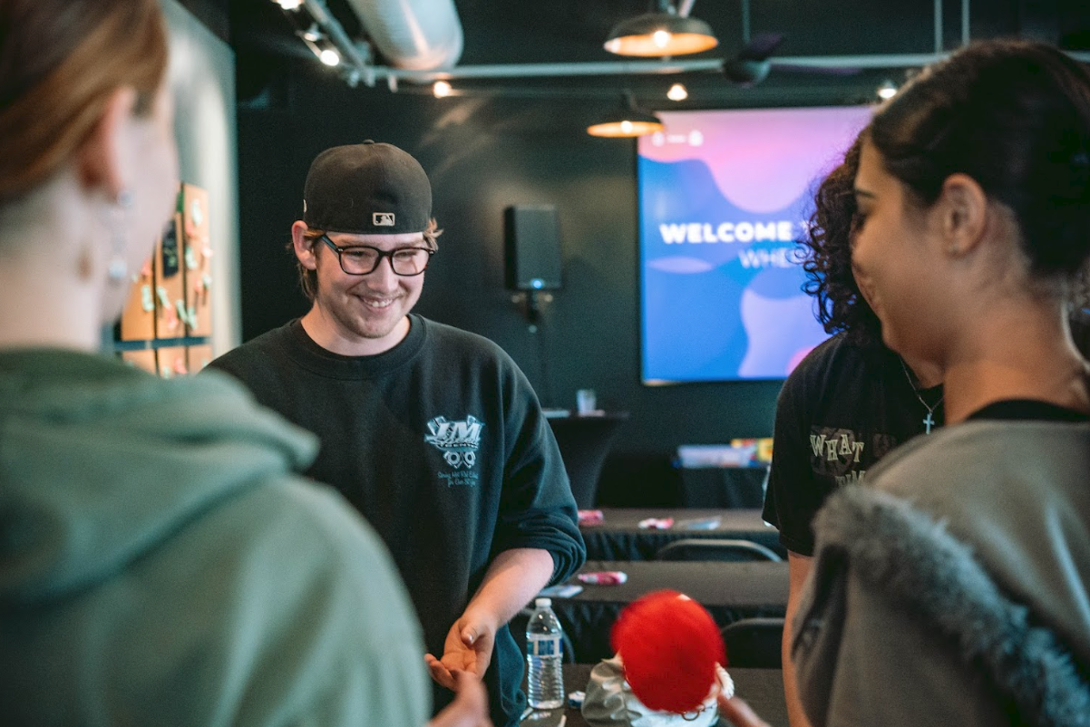 Group of people gathered in a room with a 'Welcome' sign on a screen in the background, engaging with each other and smiling.