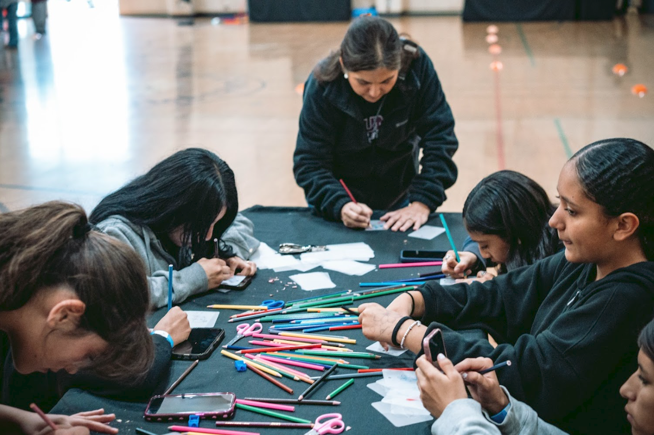 Group of young women gathered around table with craft supplies, filling out forms and taking photos