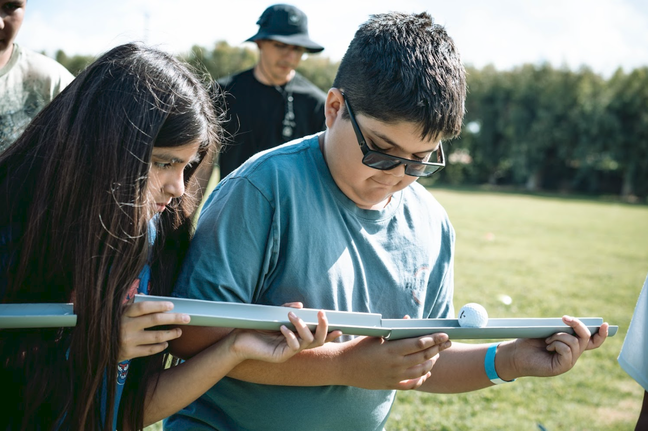 Children playing a golf mini-game outdoors on a sunny day.