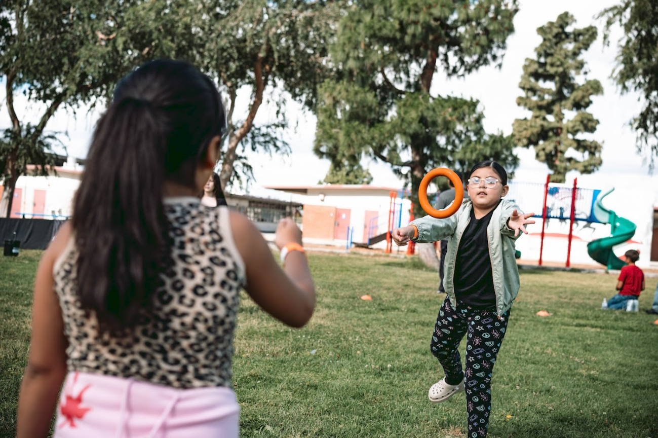 Children playing catch with rings in a park with grass and trees, a playground slide in the background.