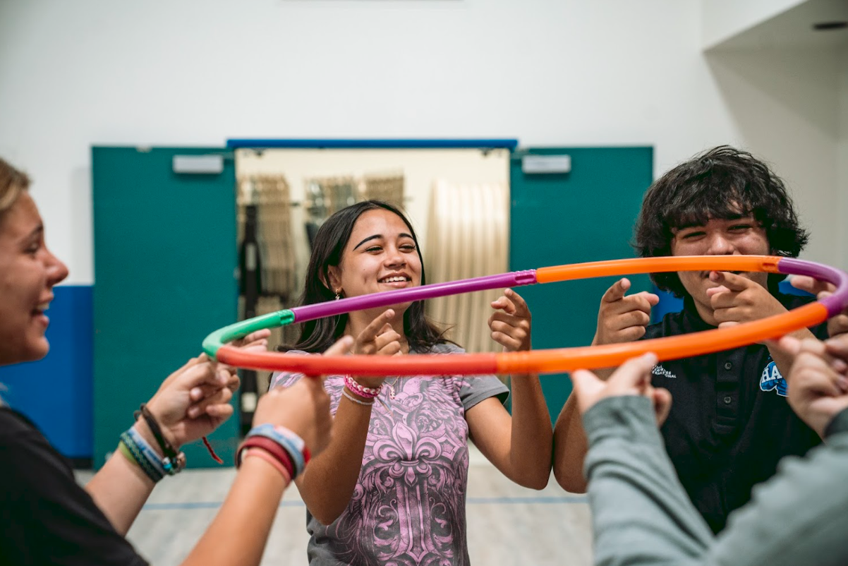 Group of smiling children and teenagers playing with hula hoops in an indoor gym or recreational center.