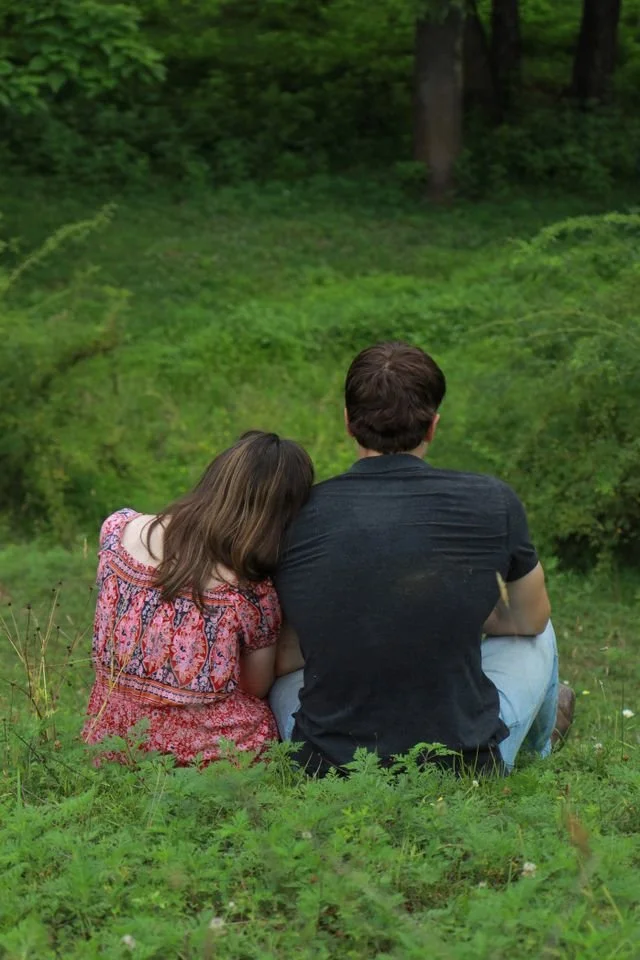 Woman leans on a man's shoulder as they sit in a green field