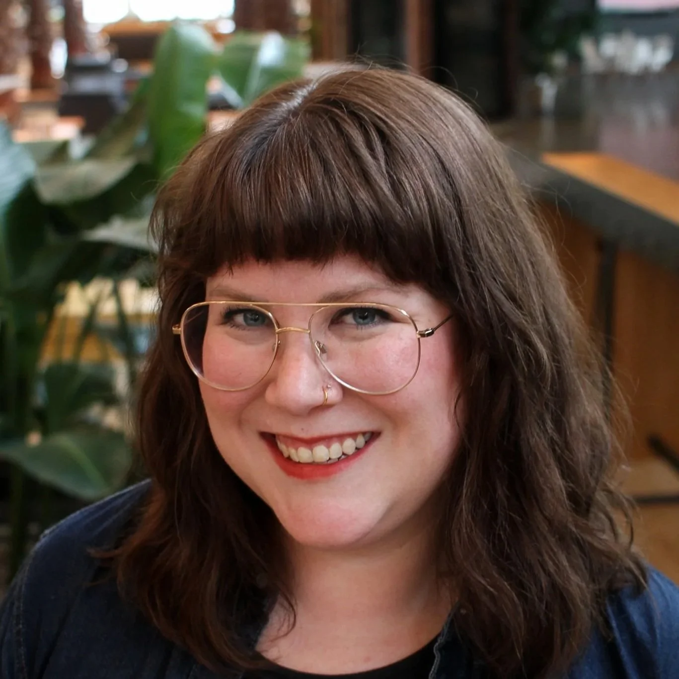 Jessie Forand with shoulder-length brown hair is standing in front of a chain link fence. She is wearing a brown cardigan over a beige and brown patterned shirt. She is smiling and looking directly at the camera.