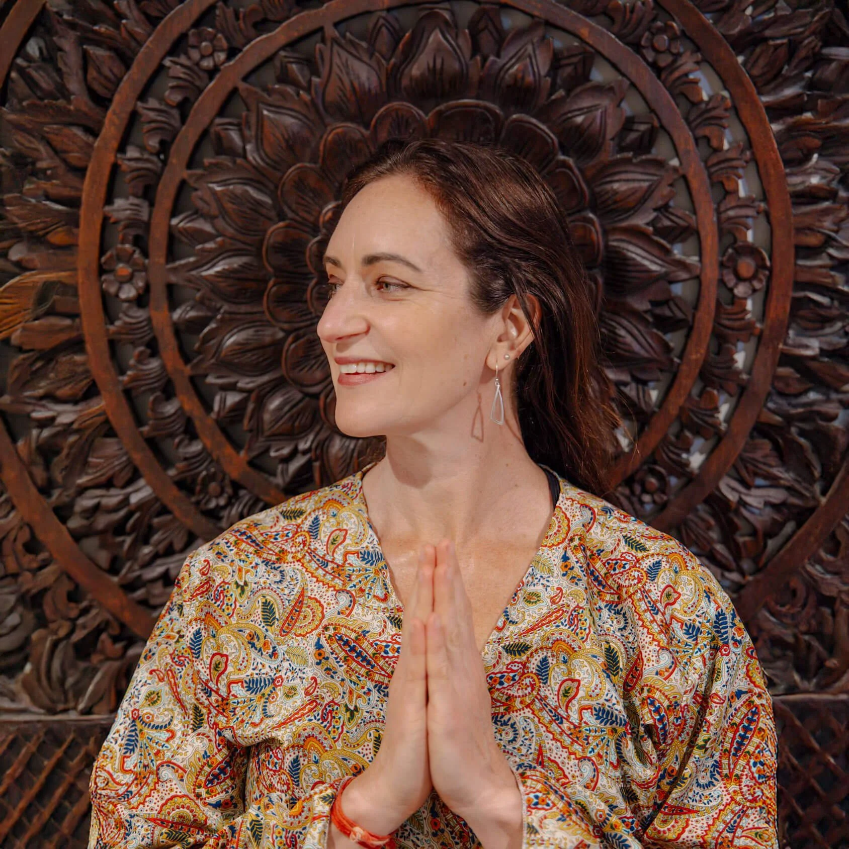 Woman practicing a headstand yoga pose indoors, with arms crossed behind her head, in a bright living room with plants and decorative elements.