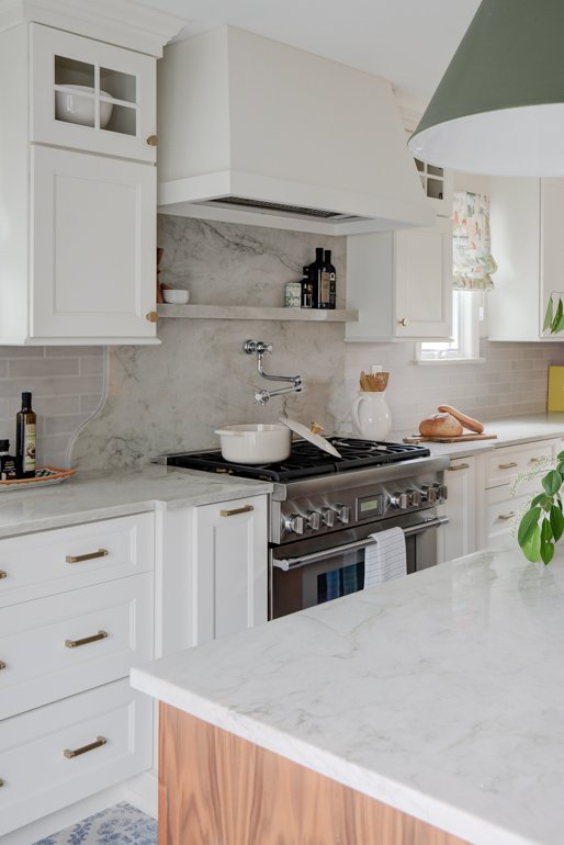 White kitchen counters and gas range with marble backsplash.
