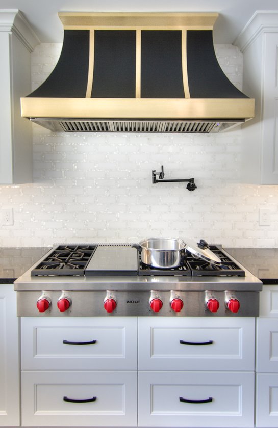 Stainless steel Wolf range under a black and gold hood.