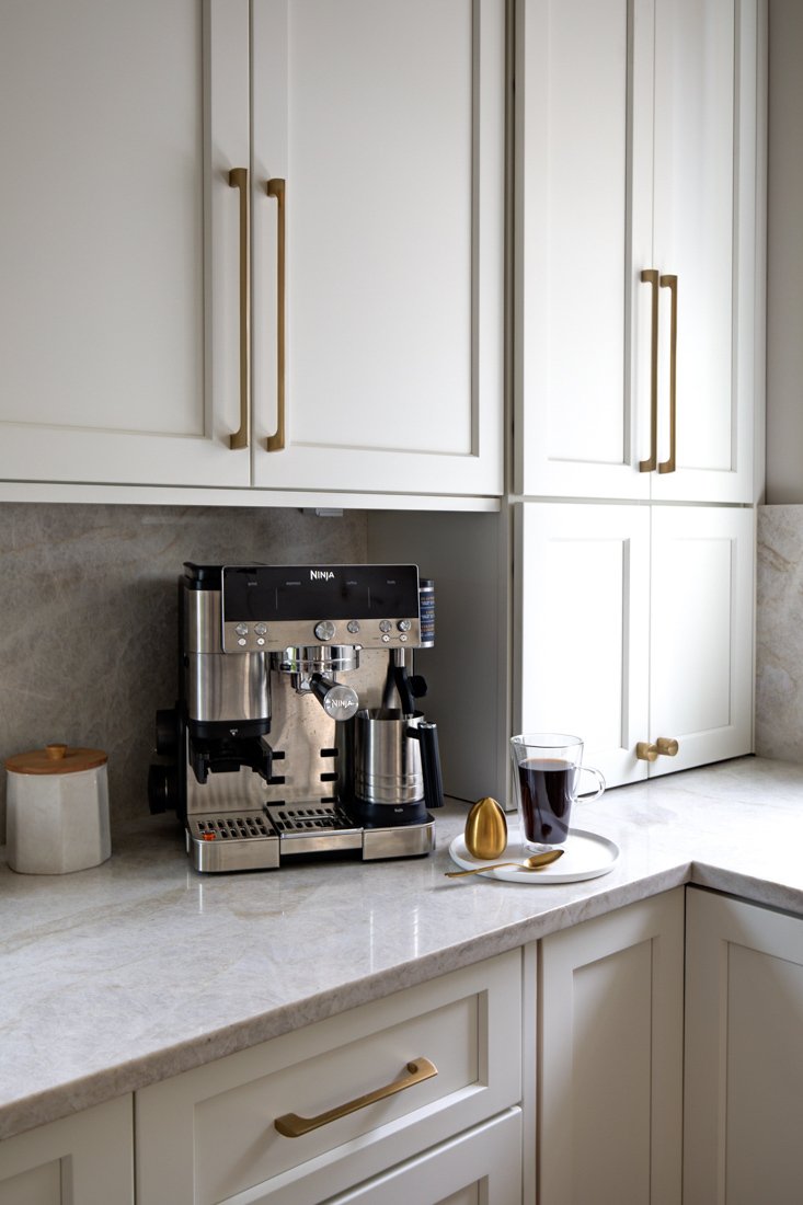 Espresso machine on marble countertop with white cabinetry.