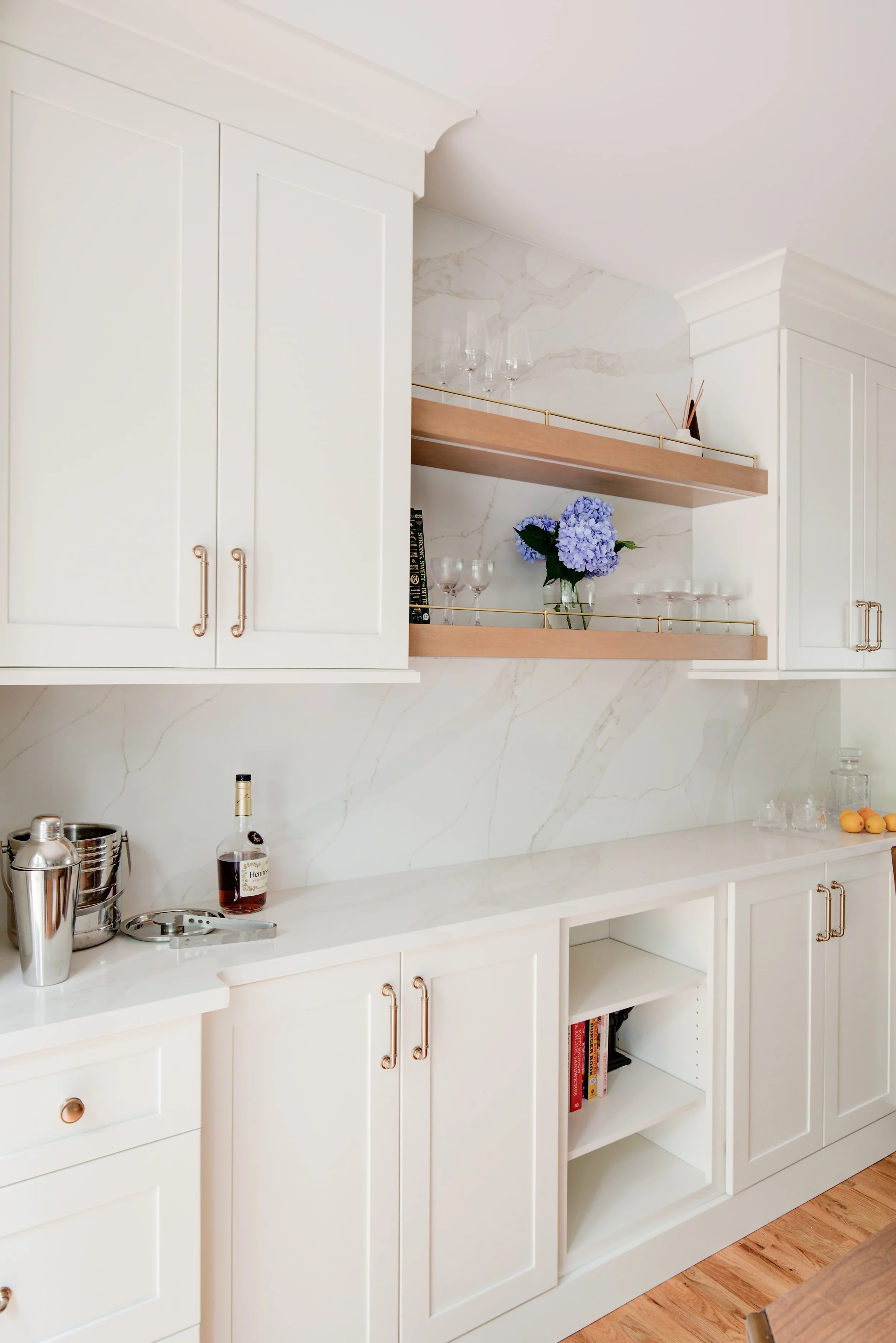 White cabinets with wooden floating shelves and marble backsplash.
