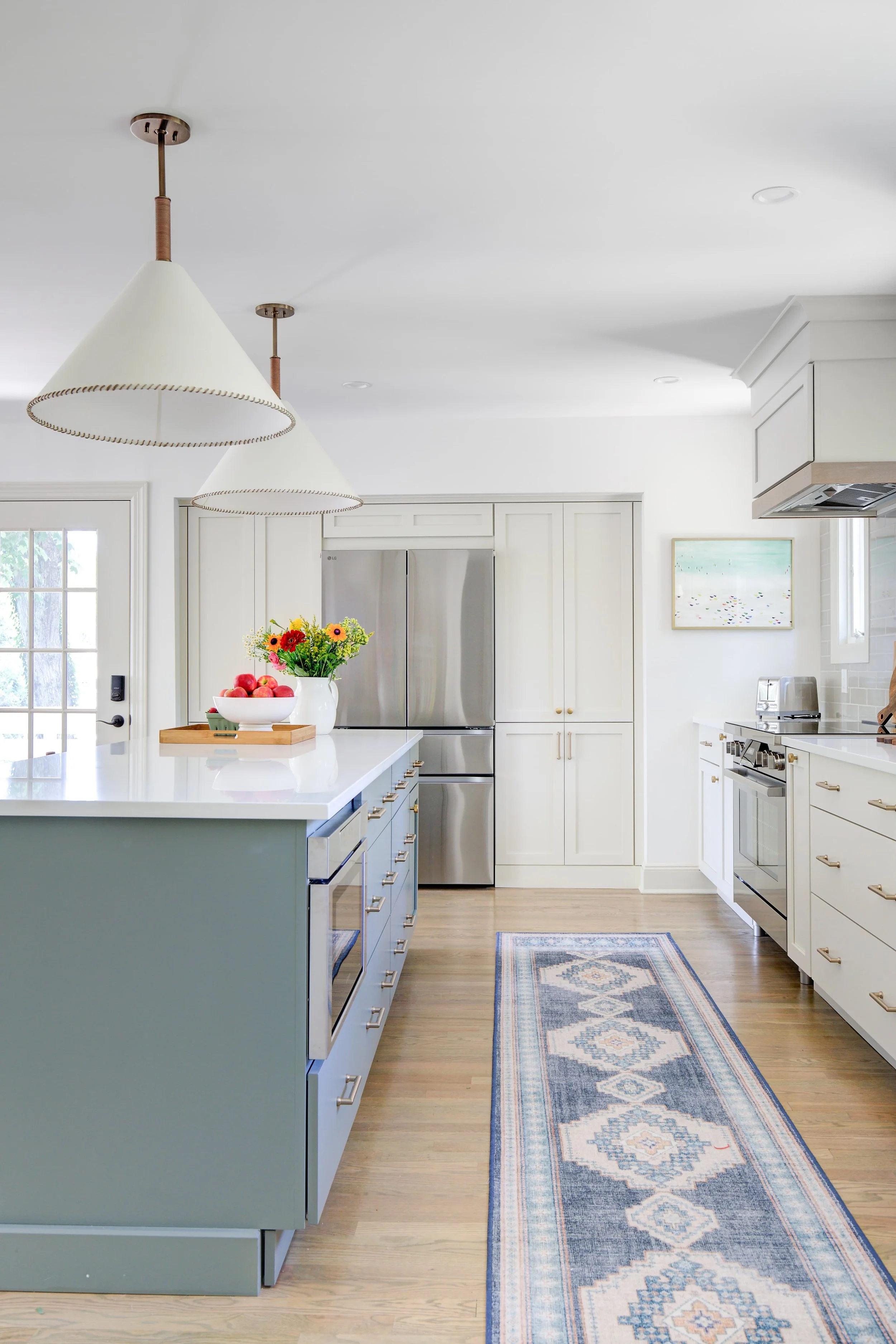 Modern kitchen with blue island, pendant lights, and runner rug.
