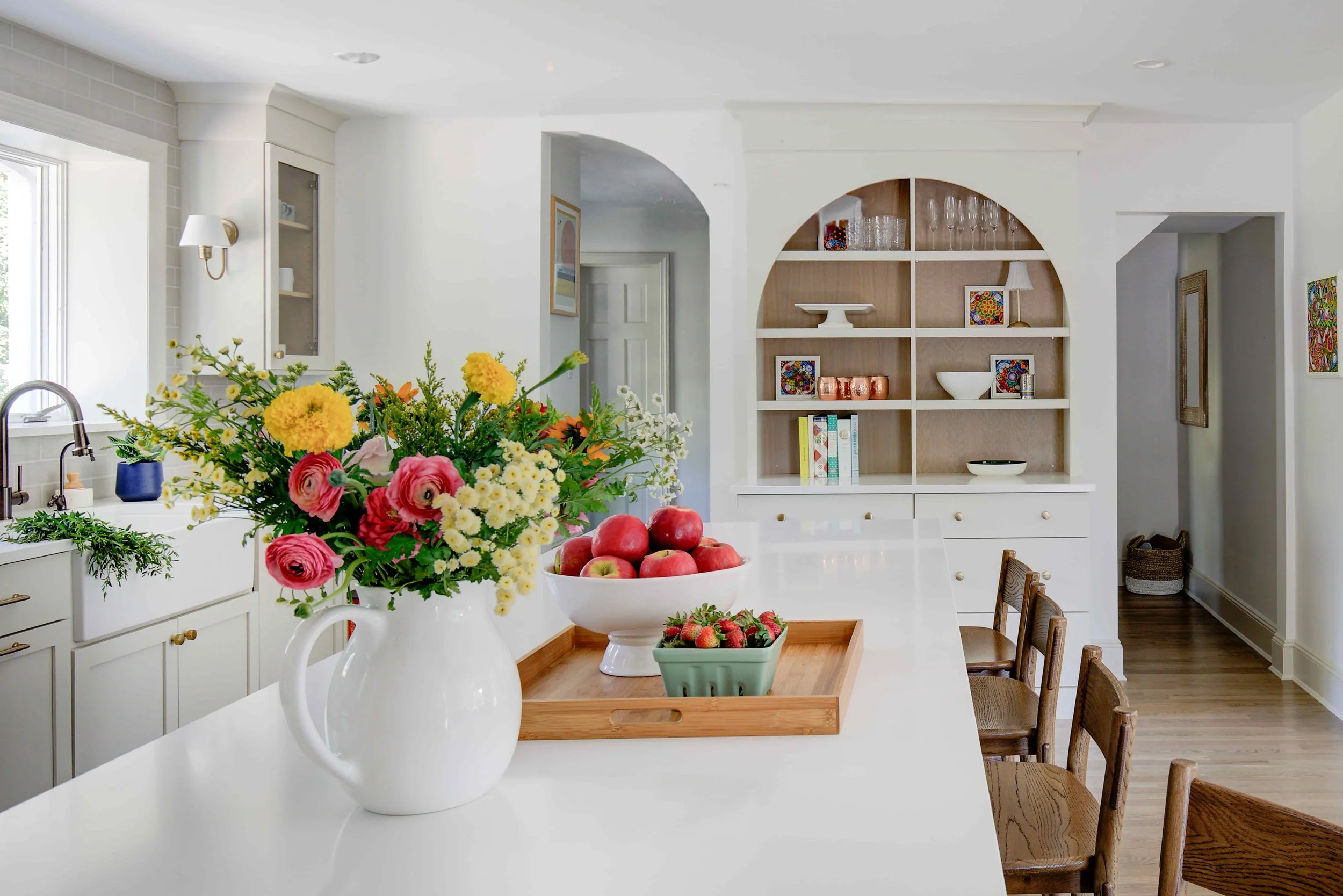 Kitchen island with flower pitcher, fresh fruit, and barstools.