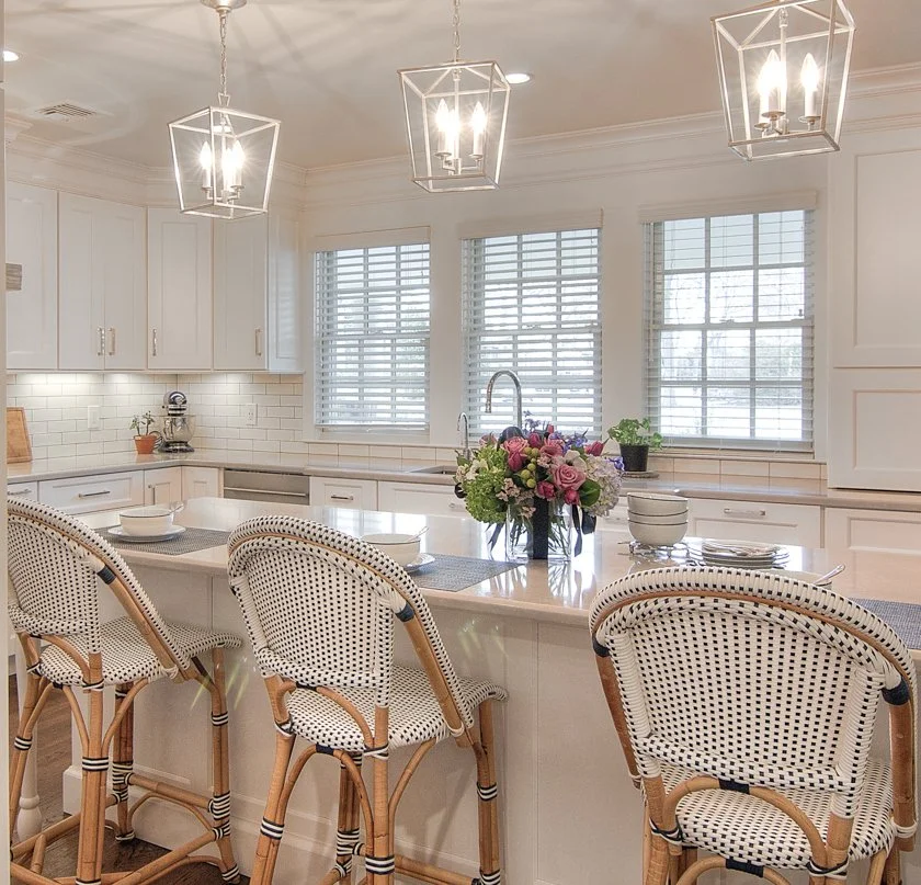 White kitchen island with three woven bar stools.