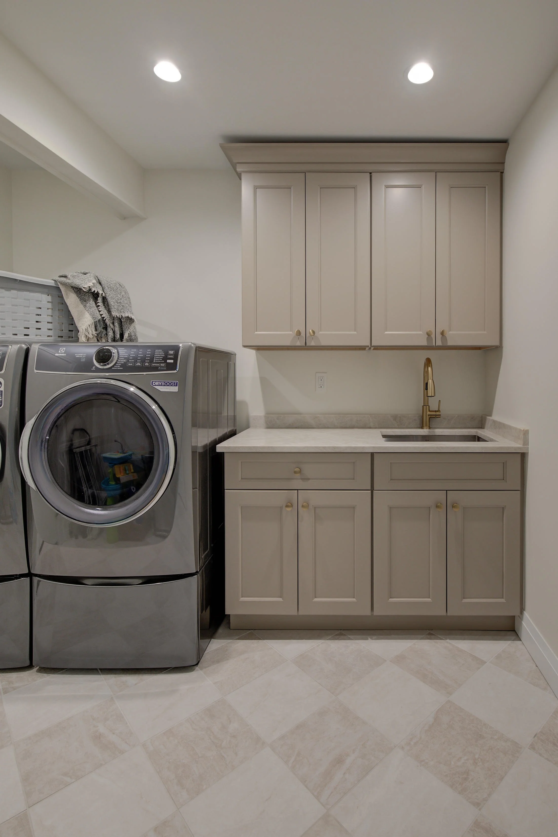 Laundry room with beige cabinets and a grey washer.