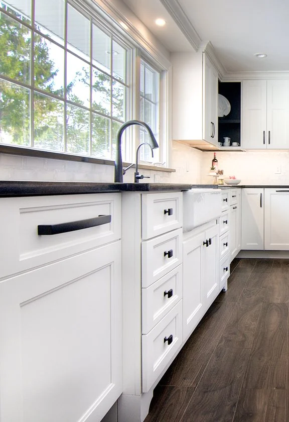 White kitchen cabinets with black handles by a window.