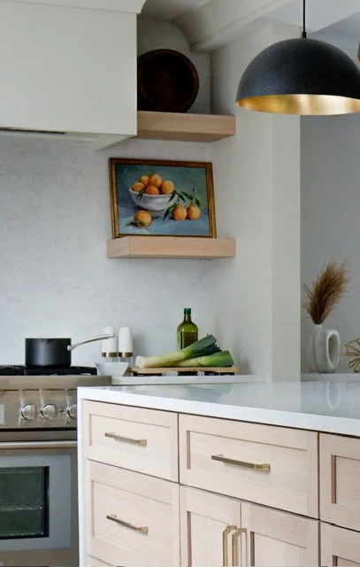 Light wood kitchen cabinets with floating shelves and artwork.
