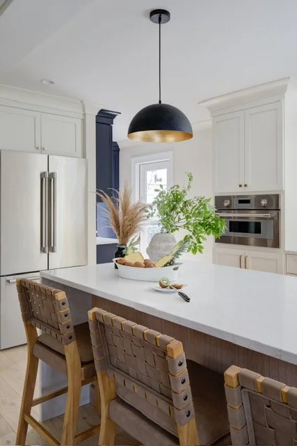 Kitchen island with white countertop, woven stools, and pendant light.