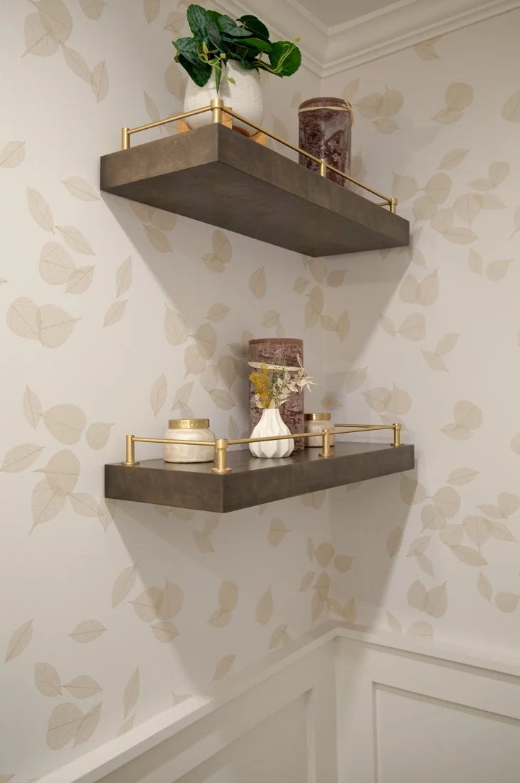 Two dark floating shelves on leaf-patterned wallpaper.