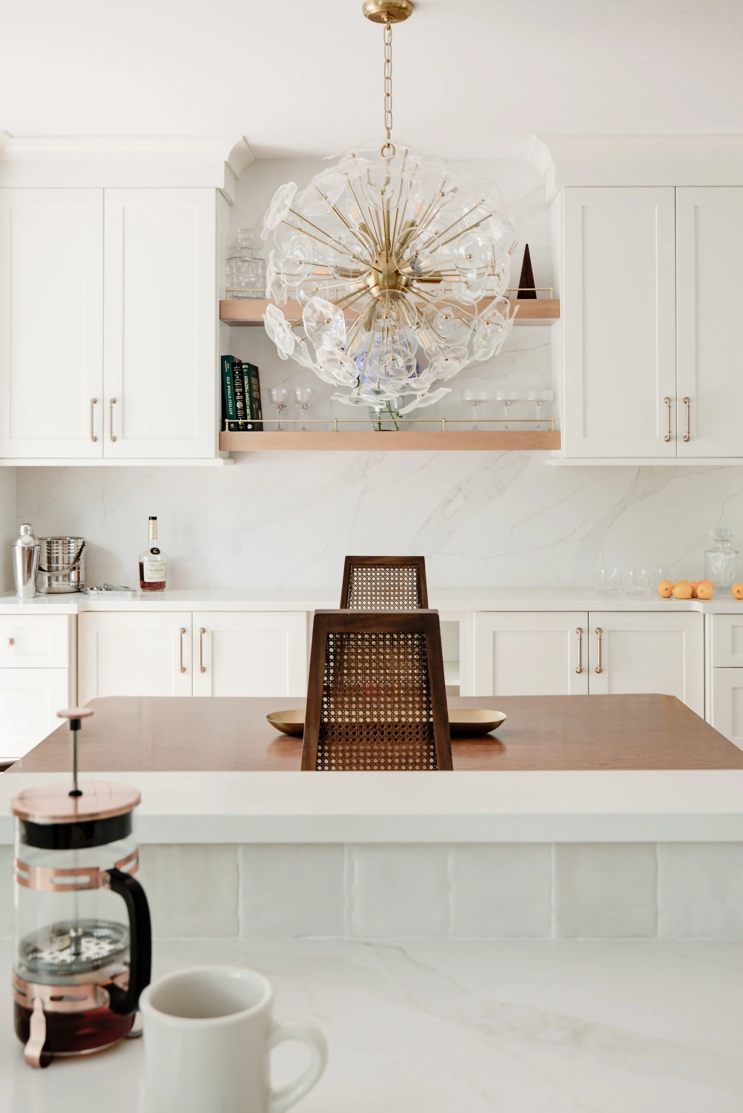 White kitchen counter with hanging glass chandelier above table.