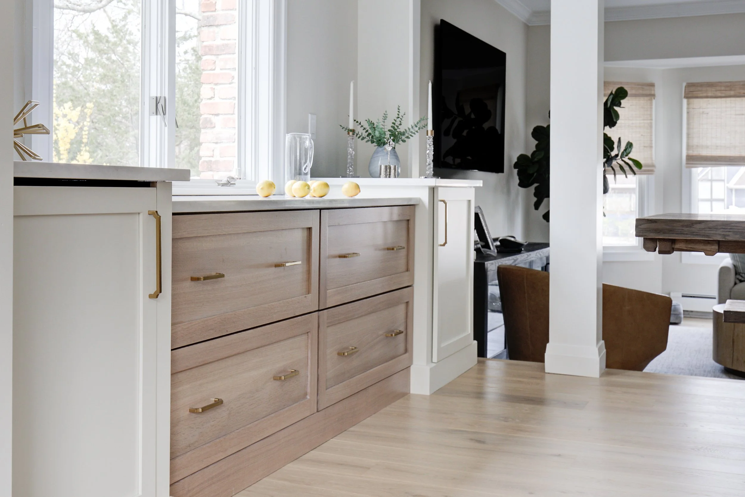 Light wood kitchen cabinets with brass hardware near a window.
