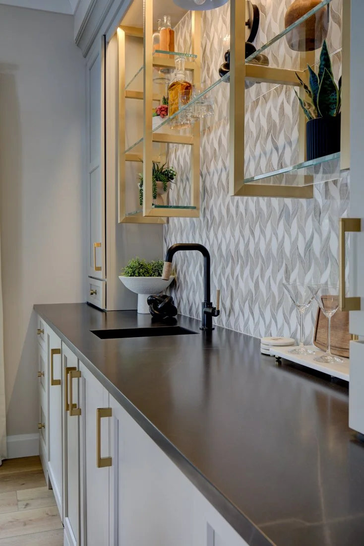 Wet bar with black sink, gold shelves, and patterned tile.