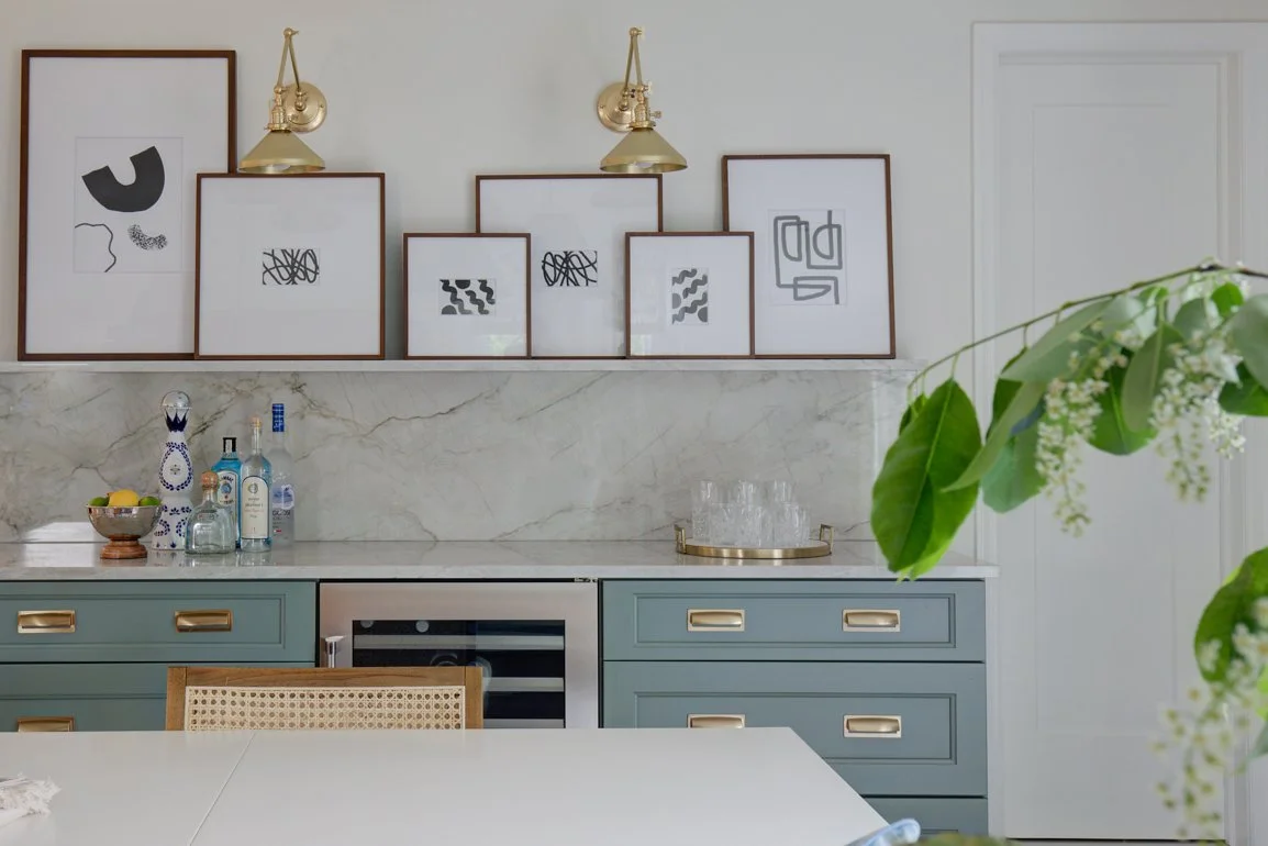 Framed abstract art displayed on a shelf above a home bar.