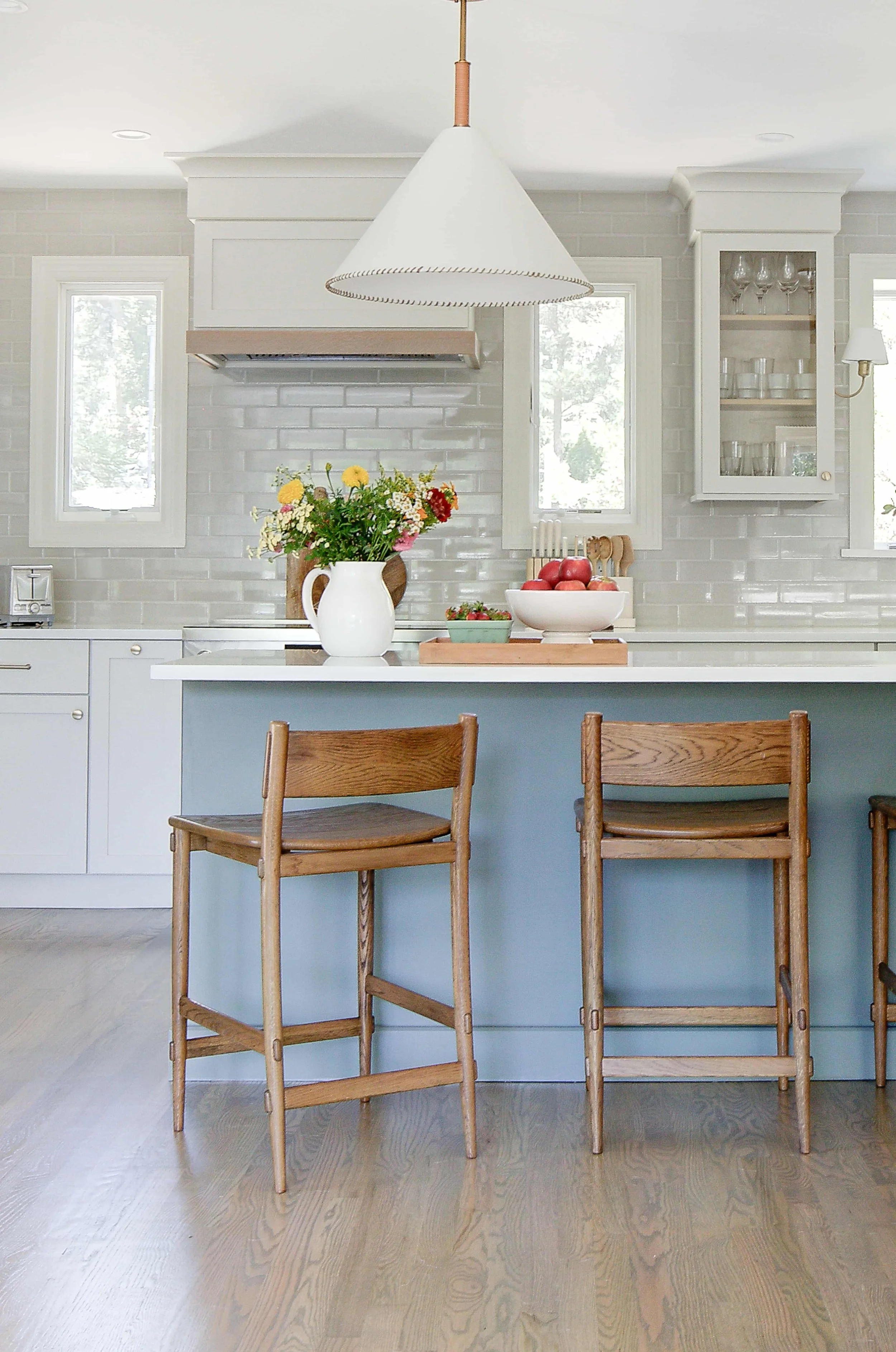 Blue kitchen island with wooden barstools and pendant light.
