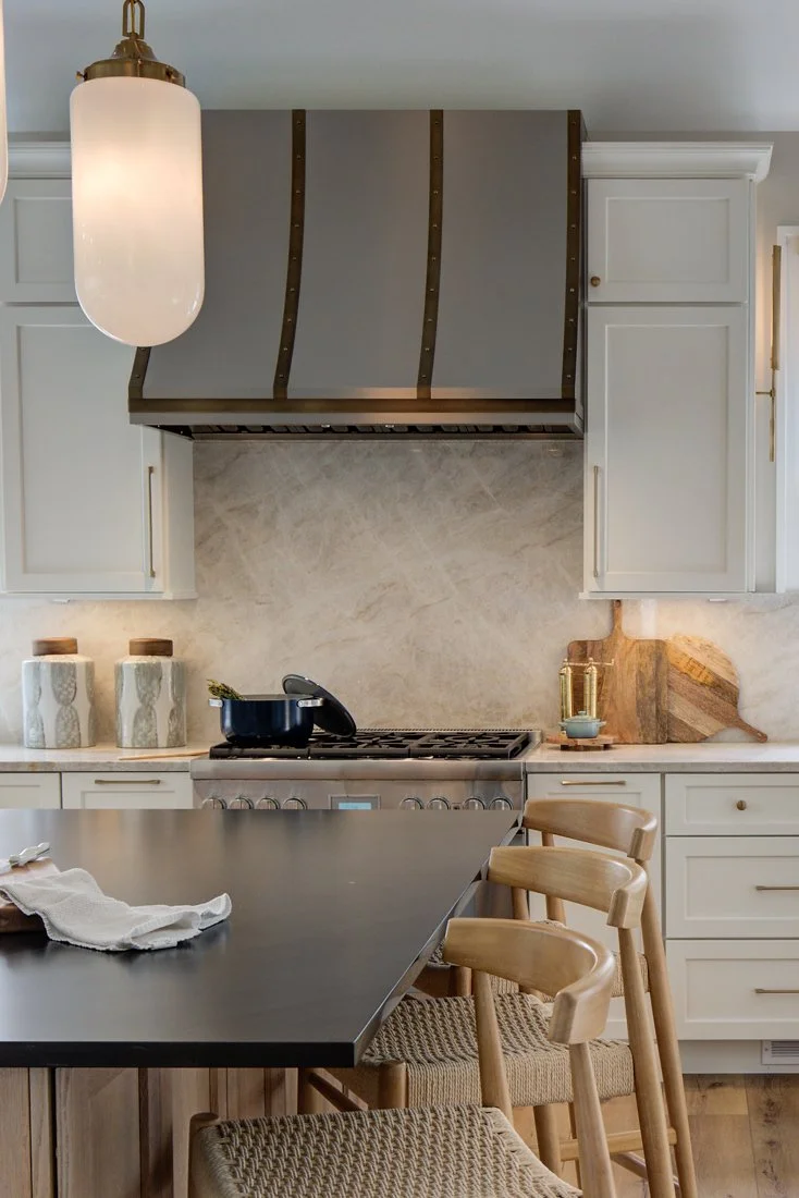 Kitchen range with large metal hood and marble backsplash.