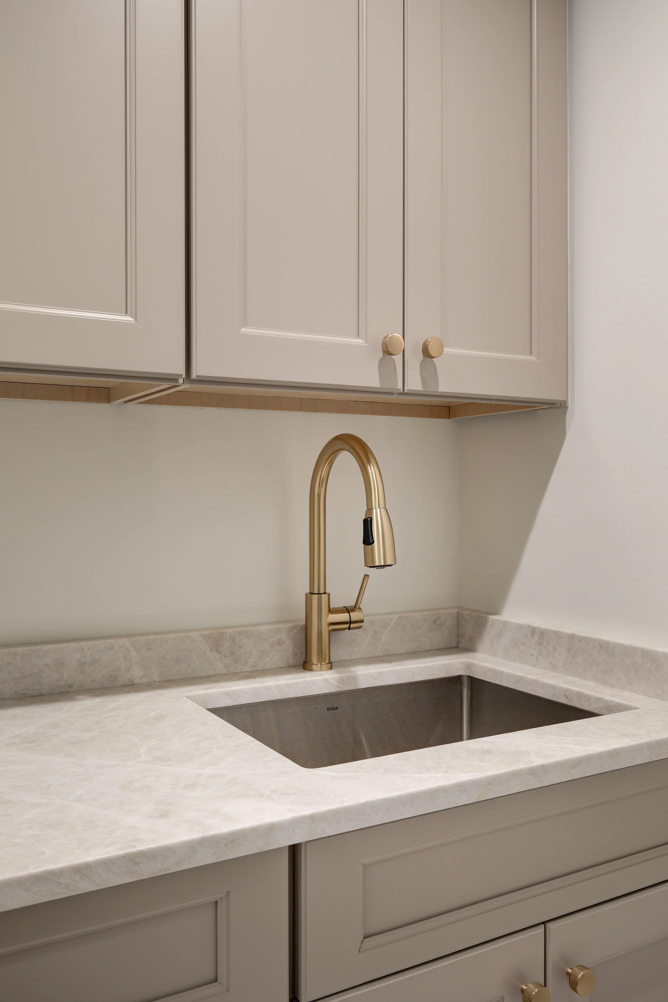 Brass faucet over stainless steel sink with marble countertop.