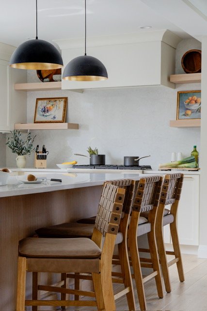 Modern kitchen featuring black pendant lights and woven barstools.