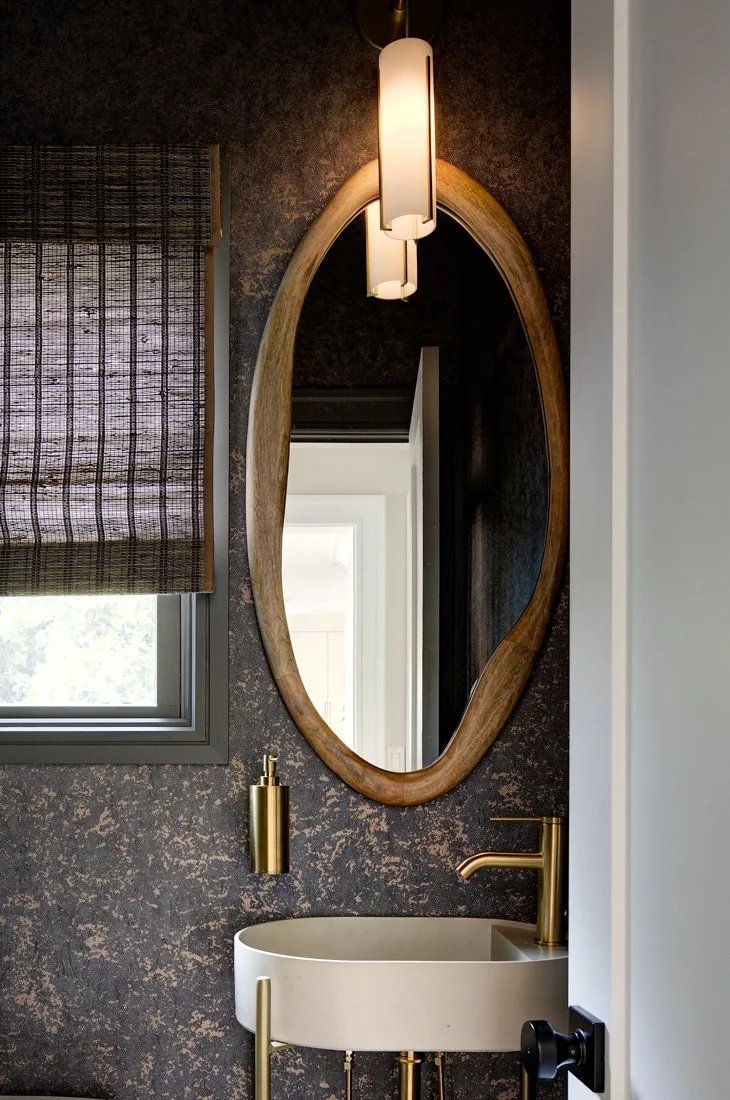 Oval mirror above a stone sink with gold hardware.