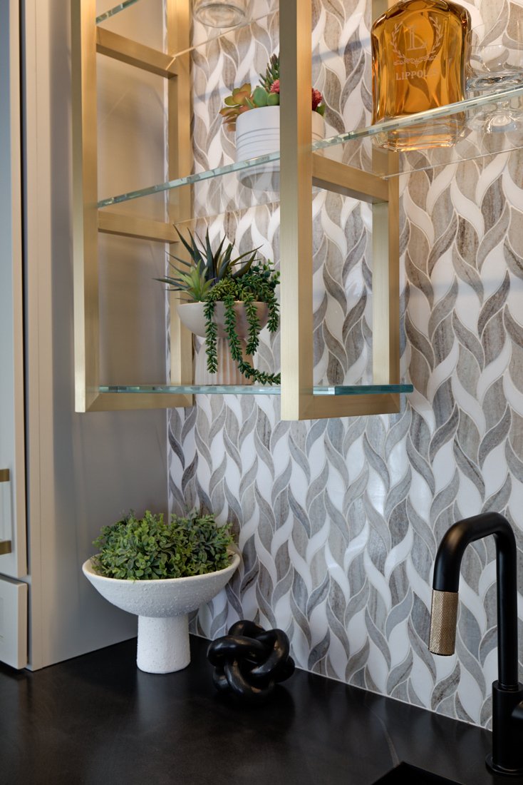 Close-up of gold shelving, patterned backsplash, and potted plants.