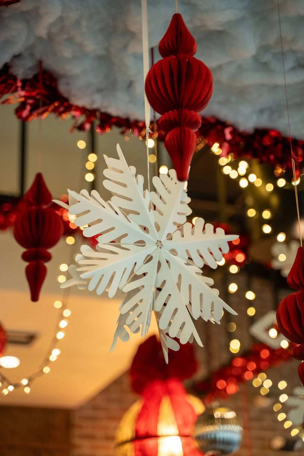 Holiday décor installation at Small Giant Christmas Bar on Water Street in Tampa, featuring hanging snowflake ornaments, red paper lanterns, and warm string lights.