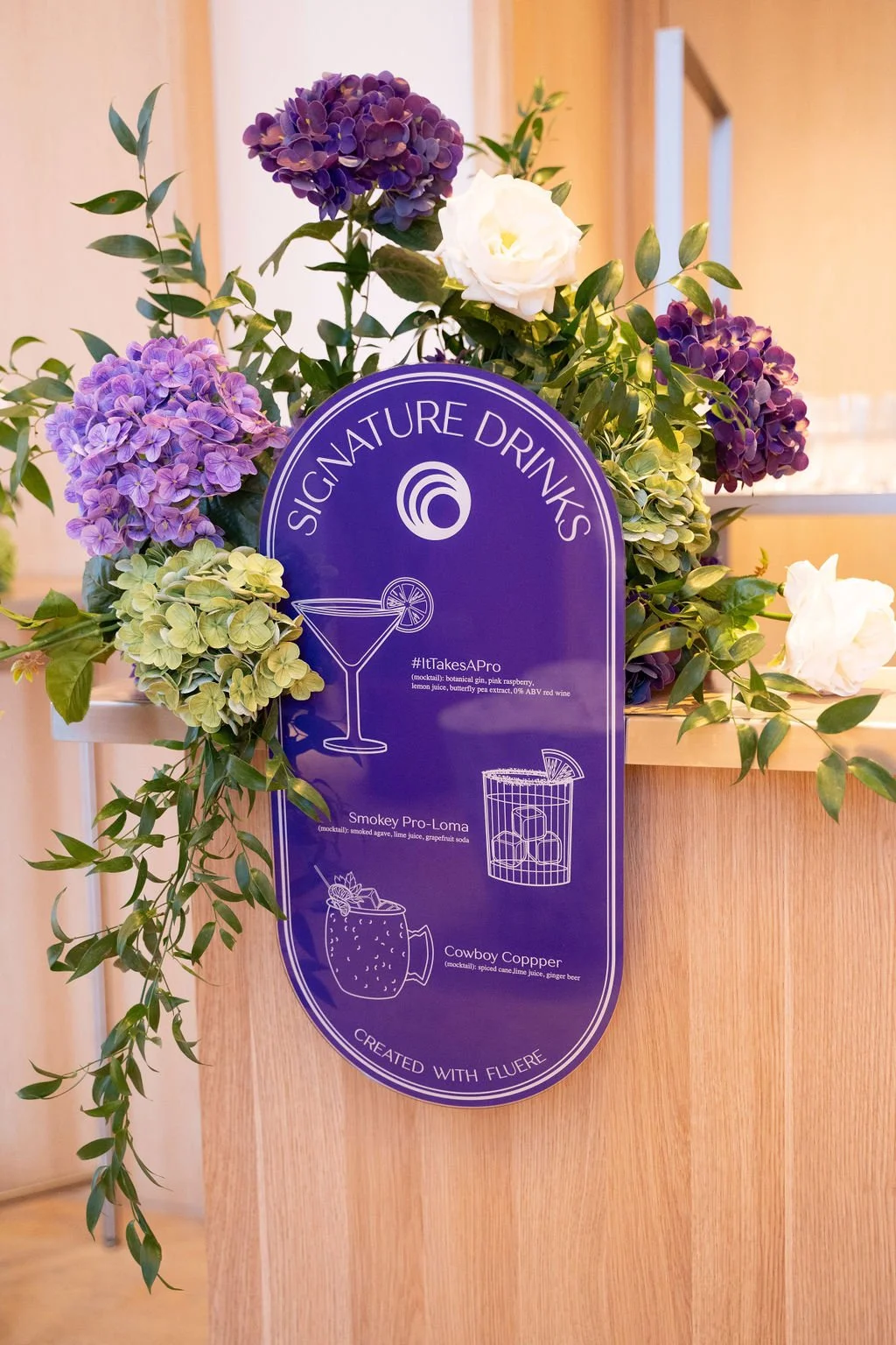 SalonCentric signature drinks menu display with floral arrangements and branded signage created in partnership with Fluère for a branded event