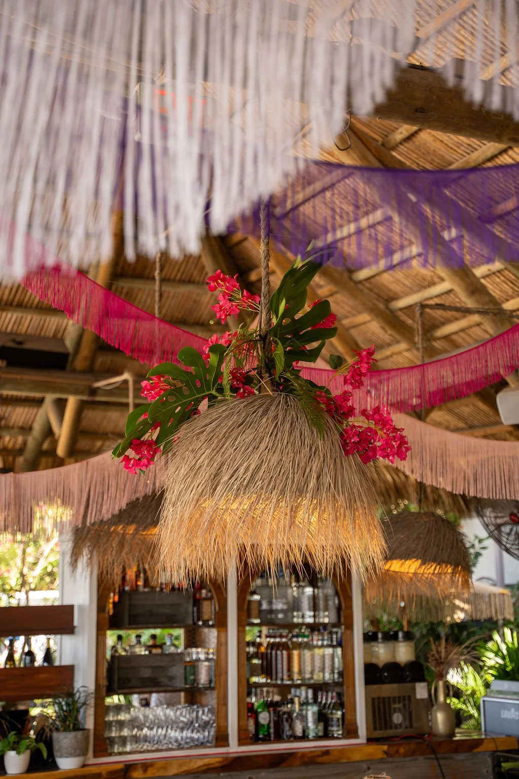 Editorial image of Joia Beach Bar in Miami styled for an F1 Welcome Party, featuring rattan dining chairs, wooden tables, and layered fringe installations in a tropical open-air setting