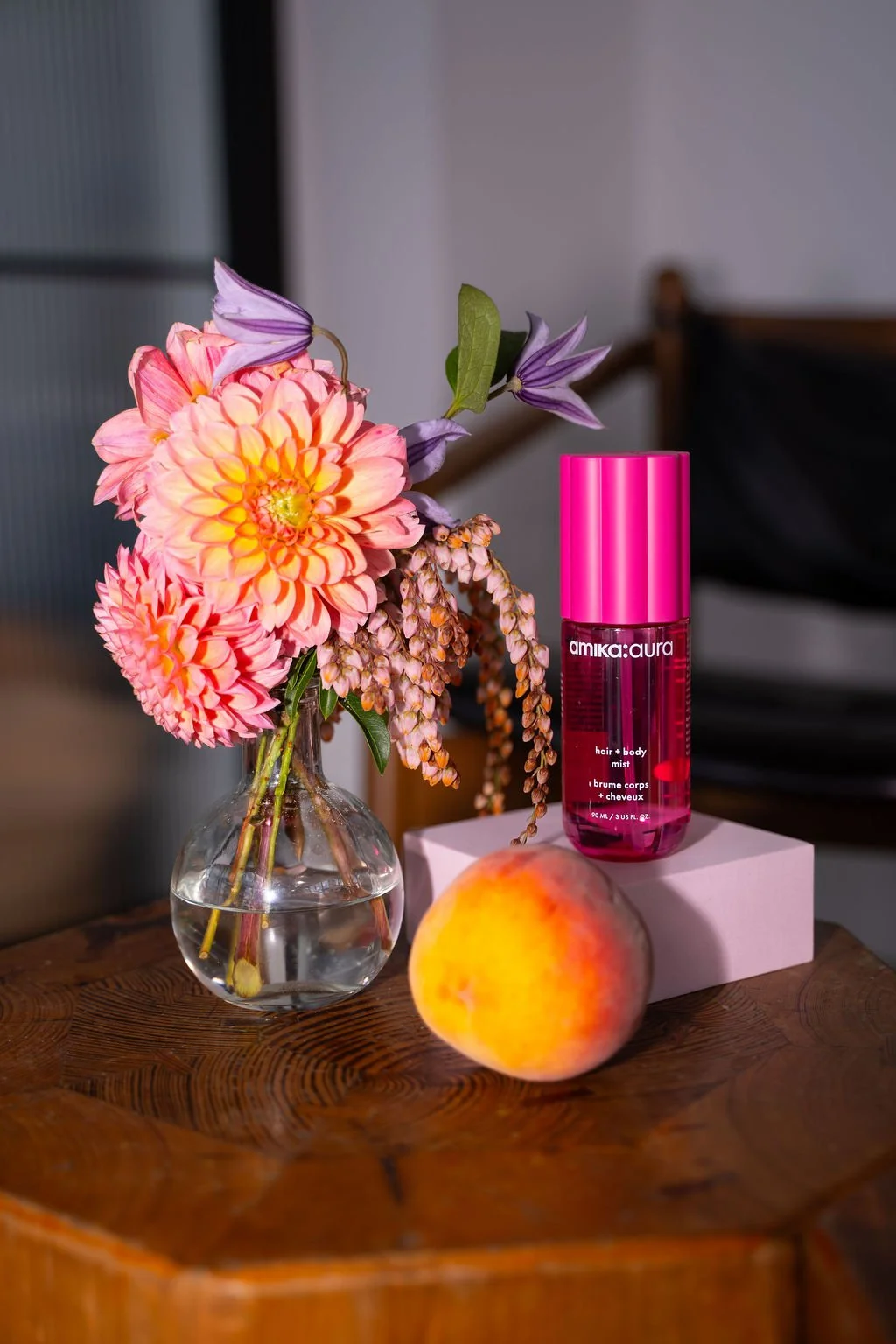 Styled product shot of amika Aura hair and body mist with fresh florals and peach accents at a Brooklyn brand activation