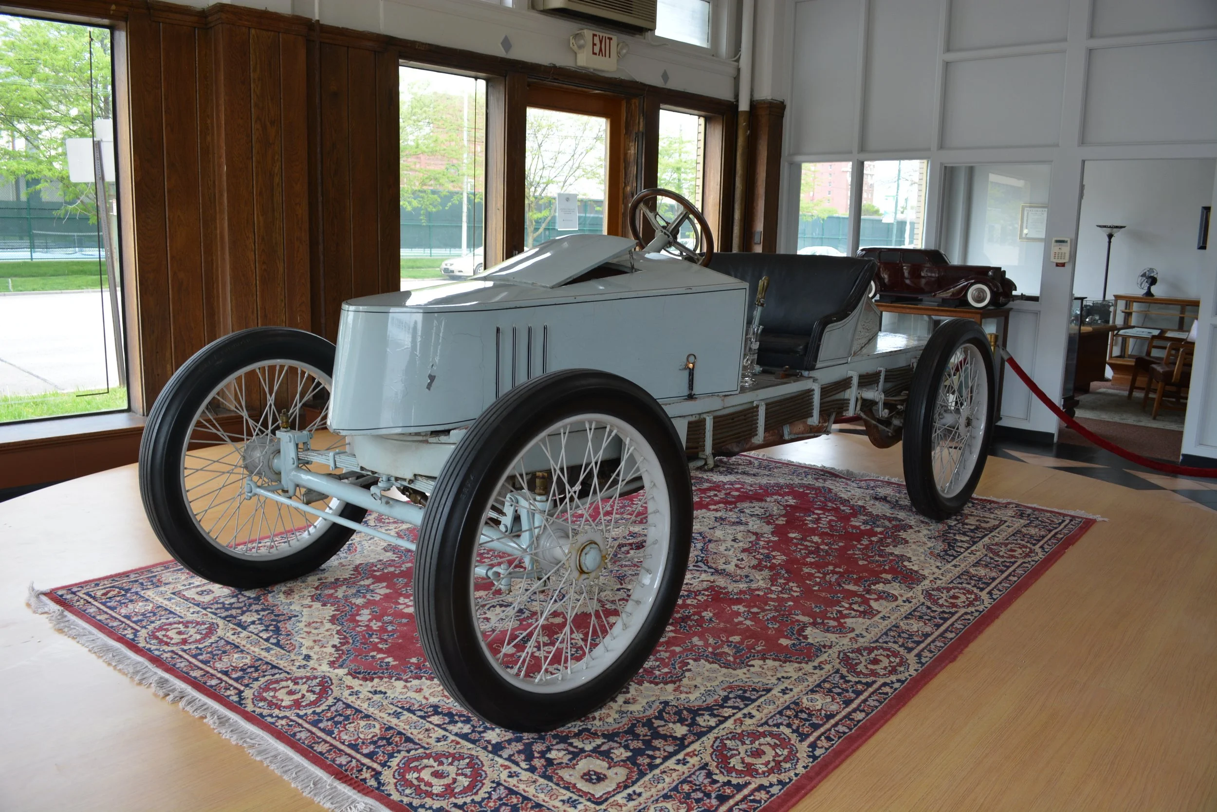 Vintage racing car on display inside a museum, placed on a decorative red and blue rug.