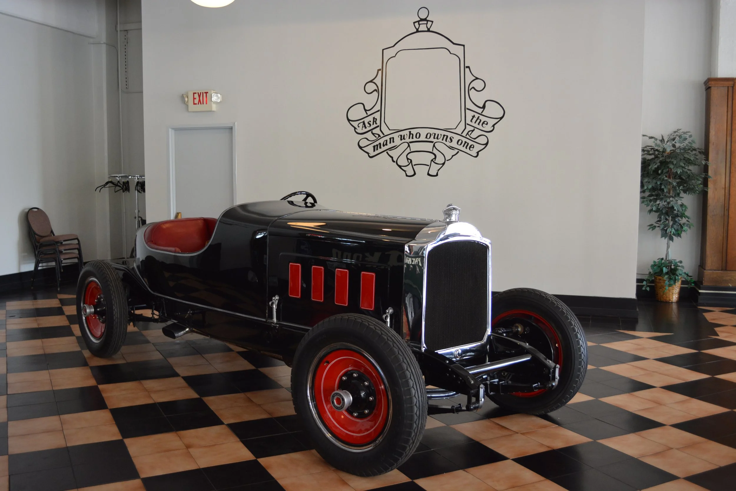 Vintage black racing car with red wheels displayed indoors on a checkered tile floor.