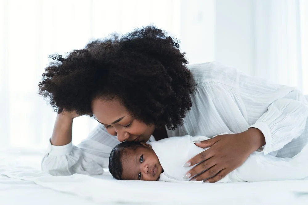 A mother laying next to he baby, kissed her head.