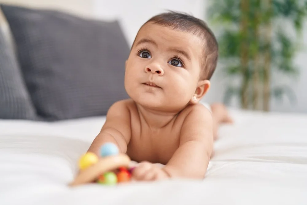 Adorable baby lying on bed holding rattle