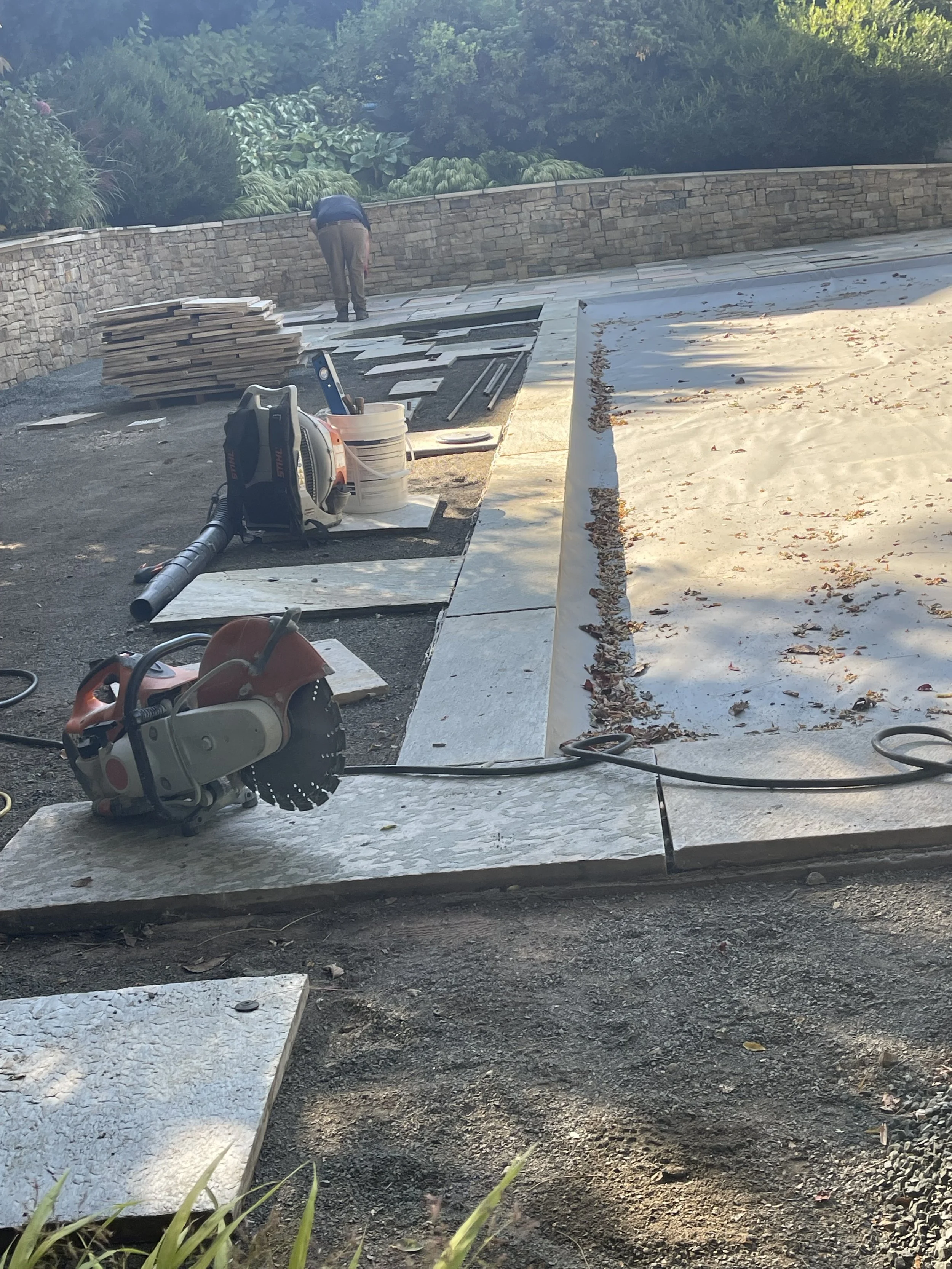 Construction workers installing large stone slabs on the ground outdoors, with tools and stacks of tiles nearby.