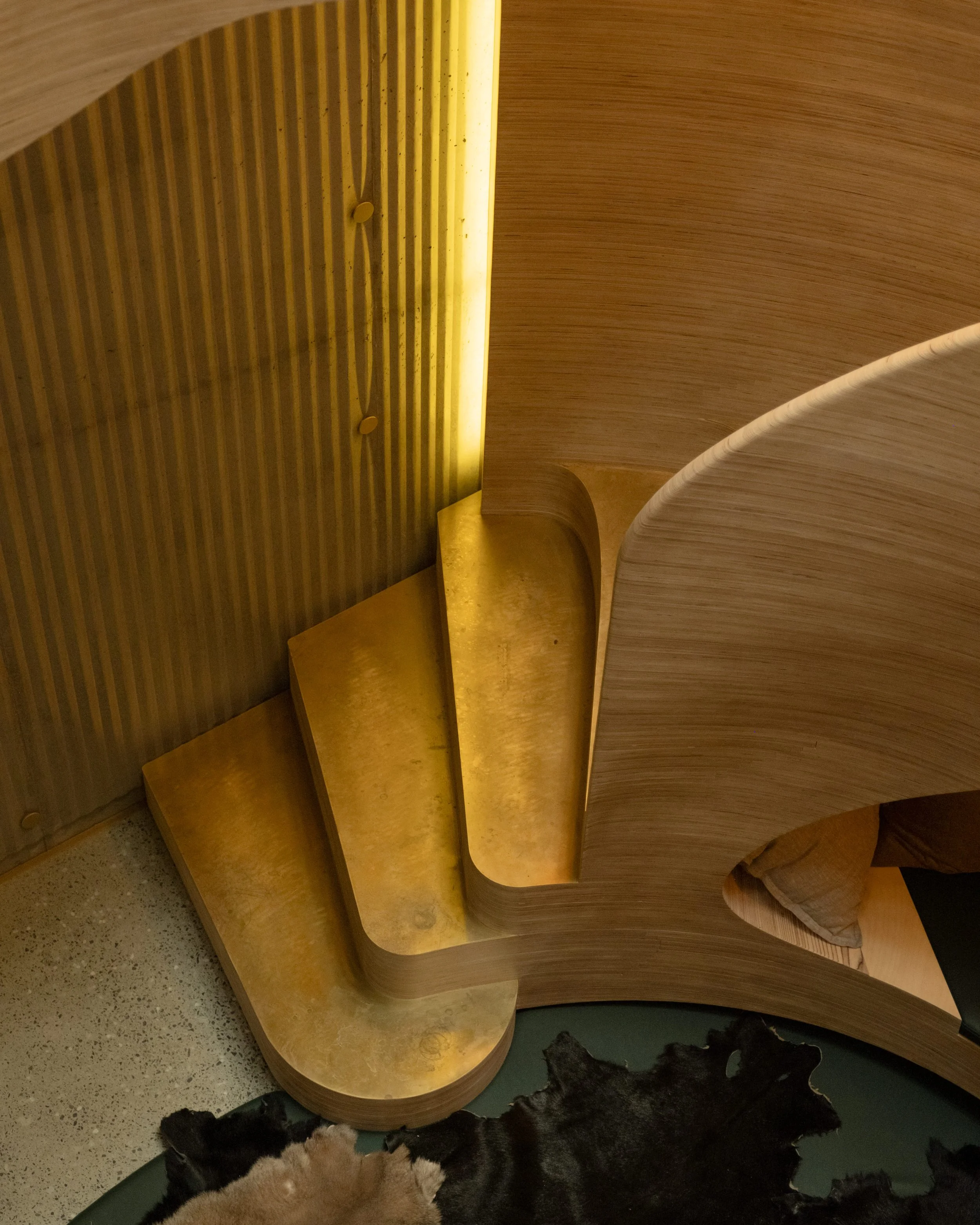 Wooden staircase with rounded edges and gold-colored steps inside a modern interior.
