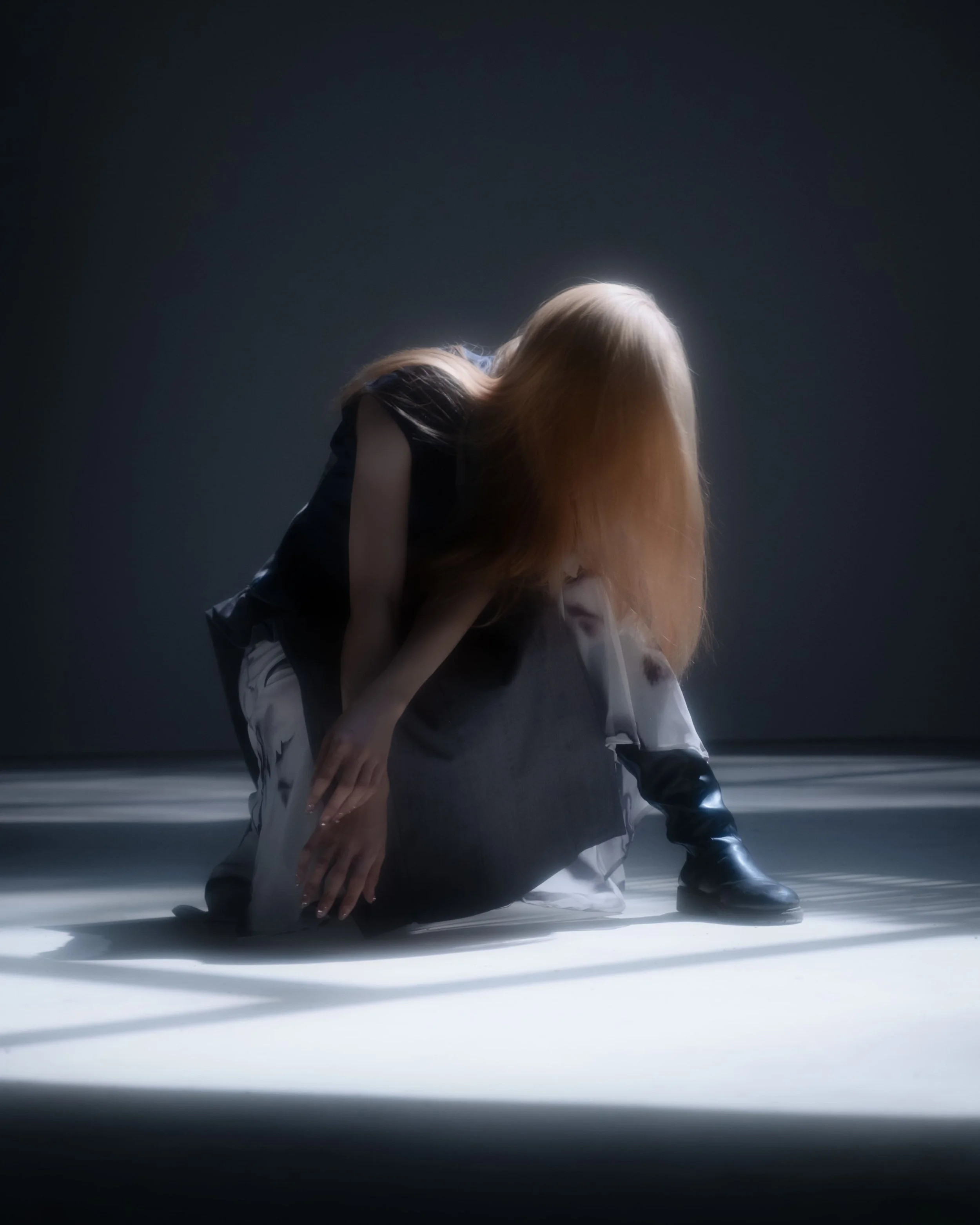 Person with long blonde hair crouching on the ground in a dimly lit space.