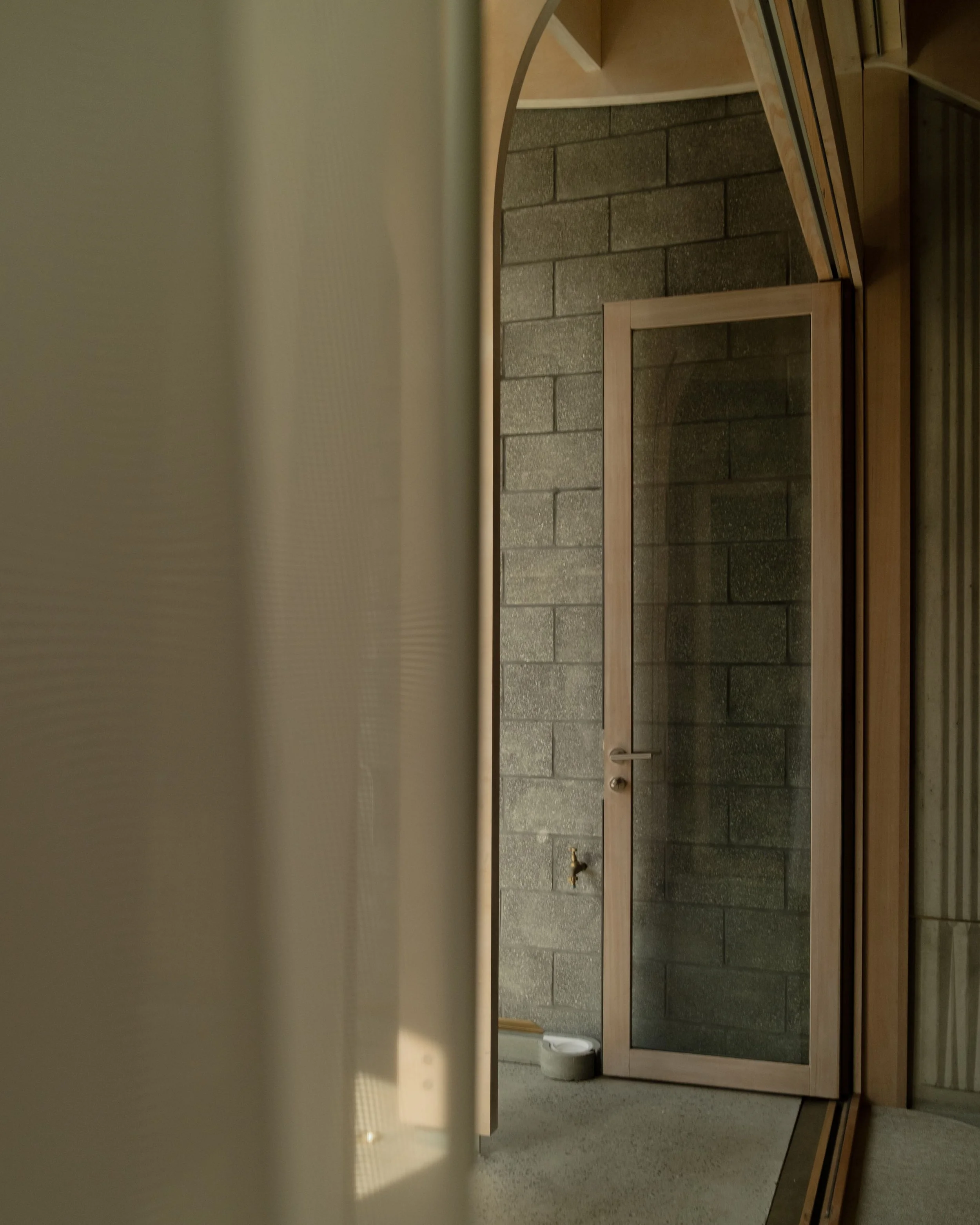 Partially open wooden door with glass panel in a room with brick wall and beige floor.