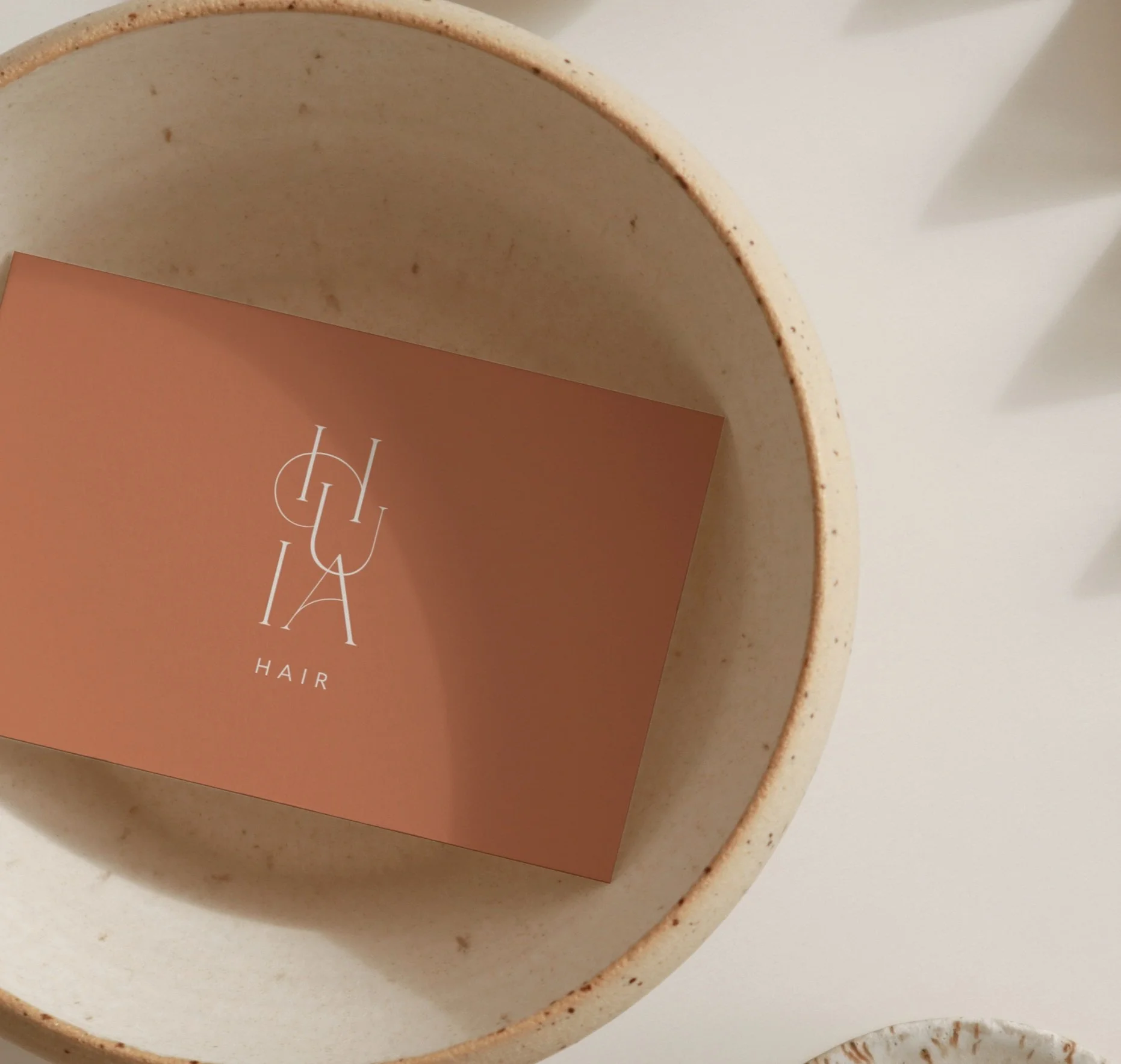 Brown business card with "CHUA HAIR" text in a beige bowl on a light surface.
