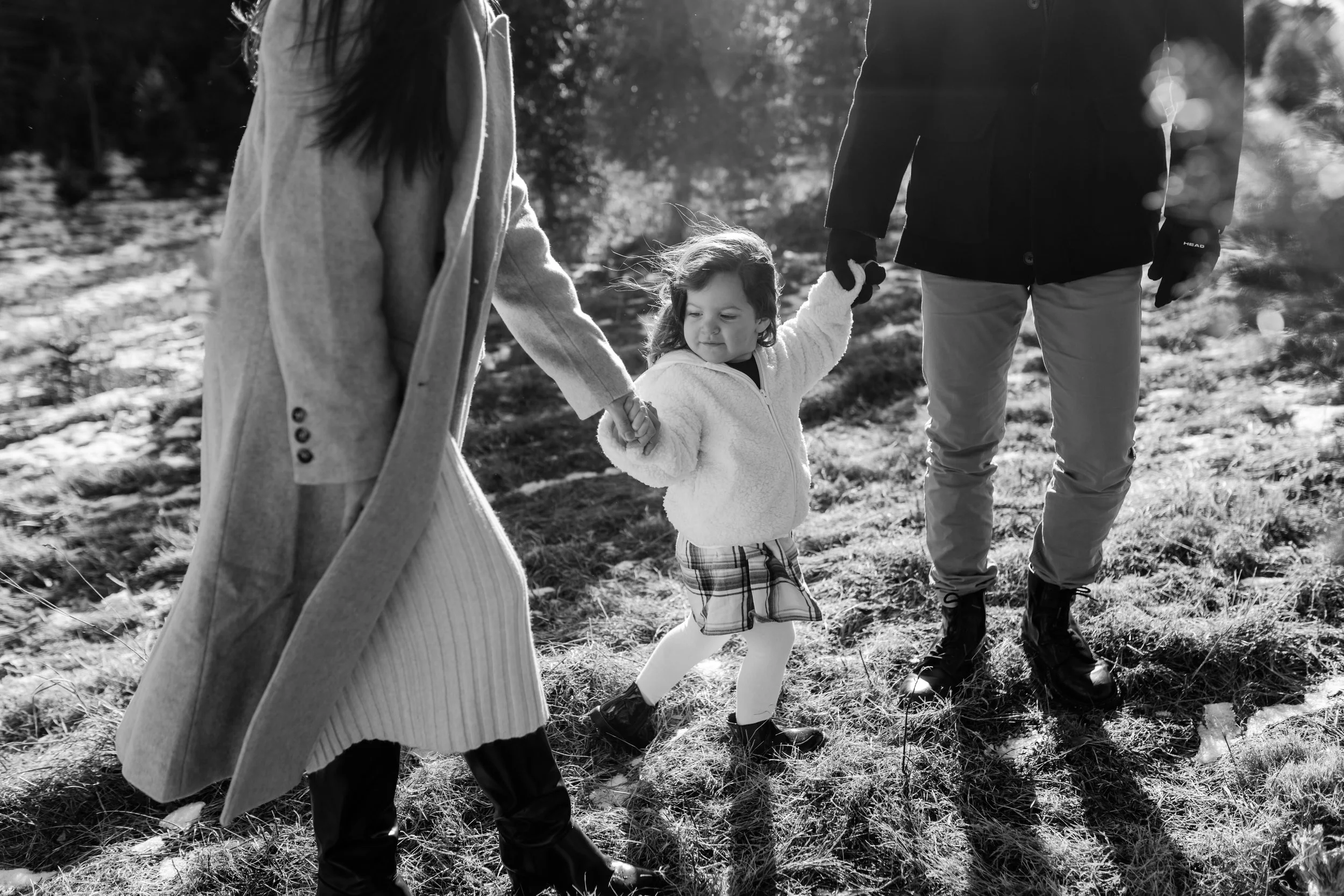 Black and white photo of a family in a field, with a child holding hands with two adults.