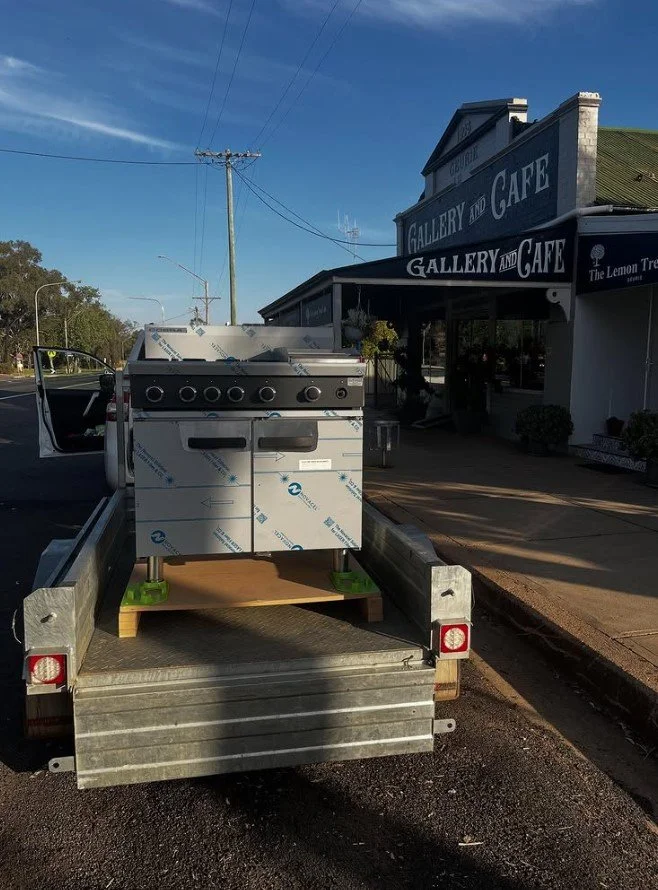 A stove on a flatbed truck parked in front of a building labeled 'Gallery and Cafe' with a small sign for 'The Lemon Tree'.