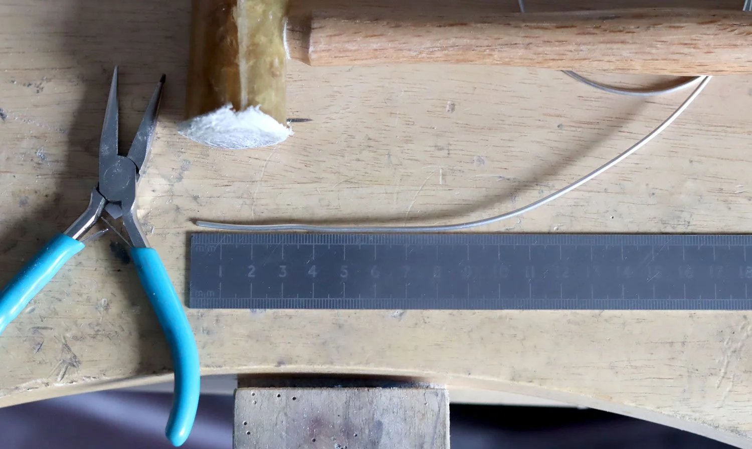 Sterling silver wire, shown next to a ruler on a workbench. Image shows pliers and a rawhide hammer.