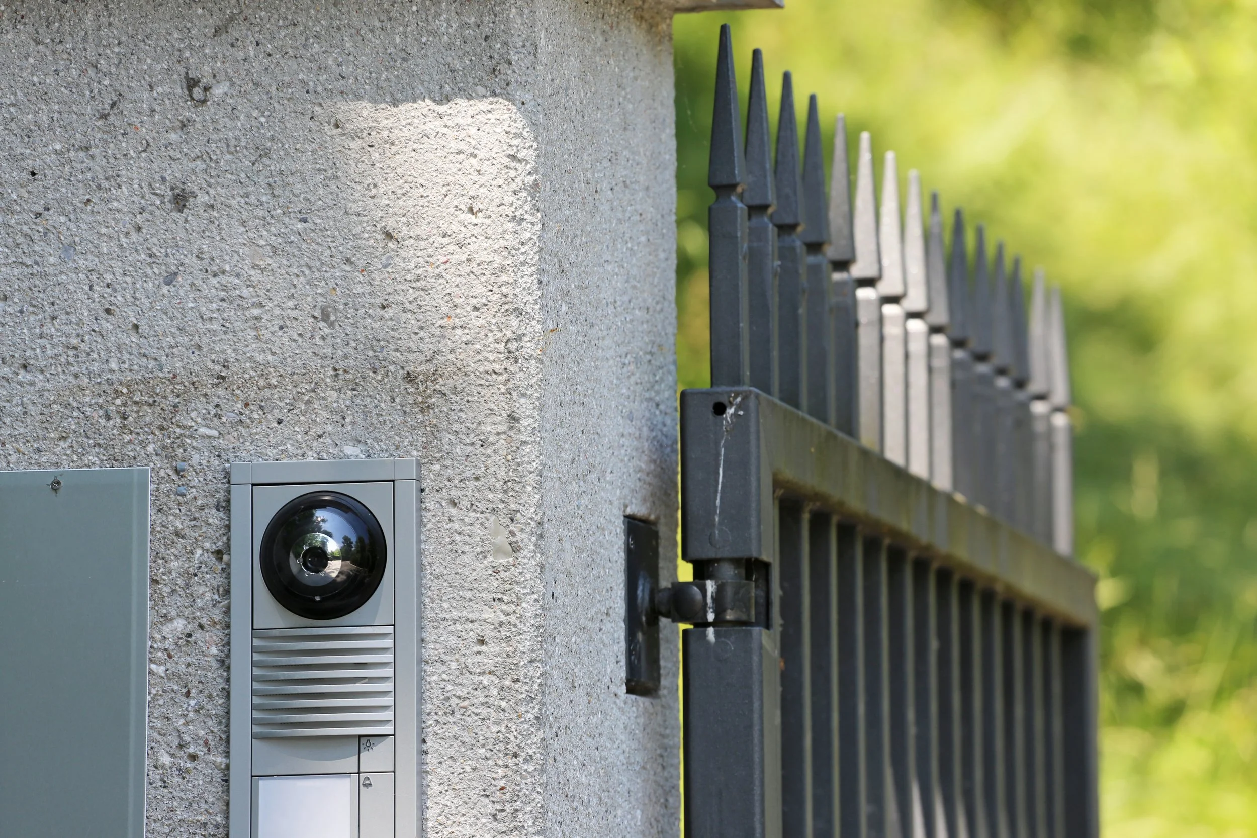 Überwachungskamera an einer Hauswand neben einem schwarzen Metallzaun.